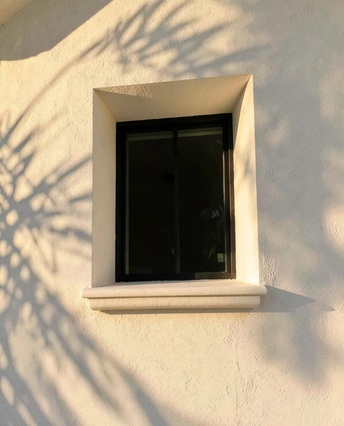 A warm white sand-finish stucco wall around a deep, crisp window opening in raking golden light (illustrative, generated).